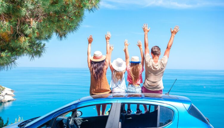 Familia con dos hijas adolescentes sobre el coche frente a la playa en la Costa Dorada